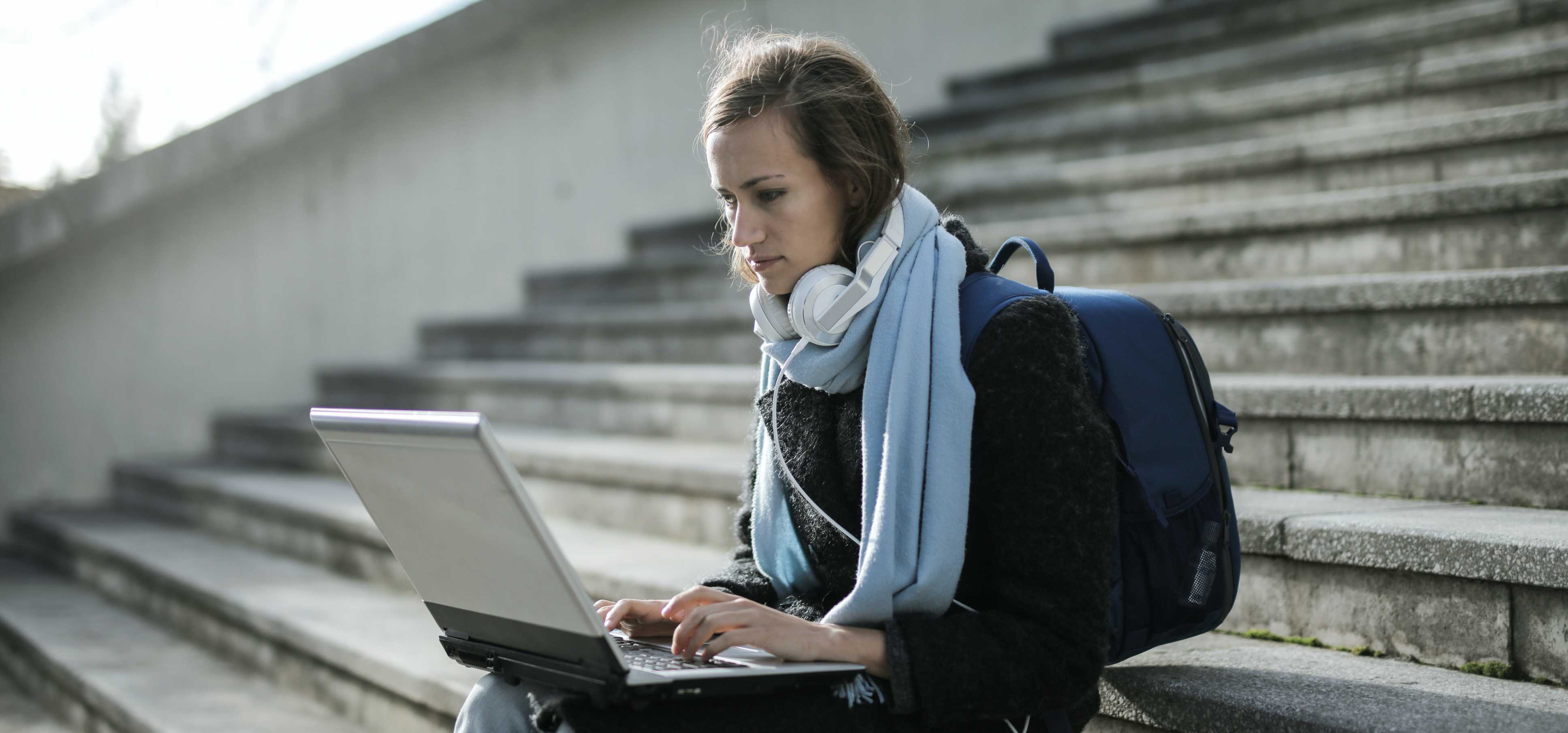 Eine Lernende mit Laptop und Rucksack sitzt auf einer Treppe.