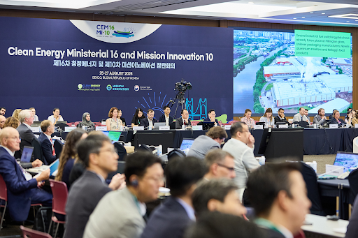 Teilnehmer beim Jubilieumstreffen sitzen an Tischen an der Wand ist ein Bild und der Name der Veranstaltung projeziert.