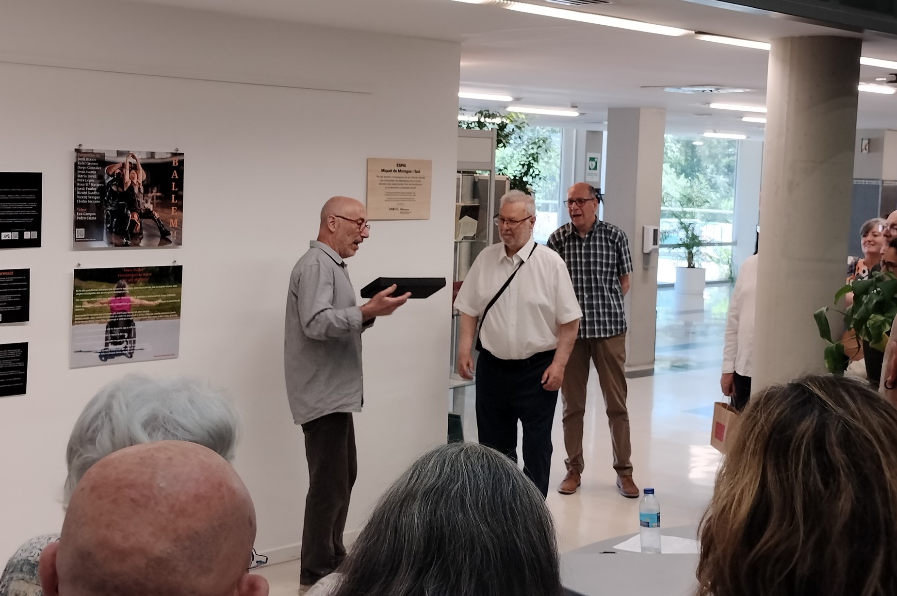 Inauguració de l'Espai Miquel de Moragas. El cap de la biblioteca, Tomàs Fabregat, lliura a Miquel de Moragas el llibre El espíritu del tiempo, d'Edgar Morin, en presència dels assistents a l'acte