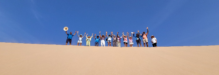 Groupe de personnes tendant les bras vers le ciel sur une dune au Maroc