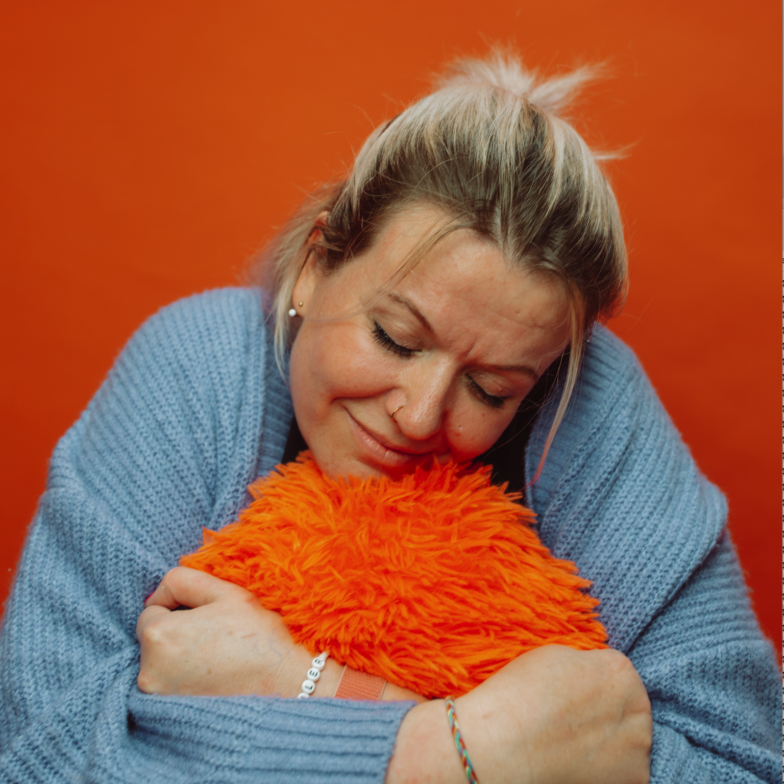 Corina Elfe vor orangenem Hintergrund mit blauem Kissen in der Hand