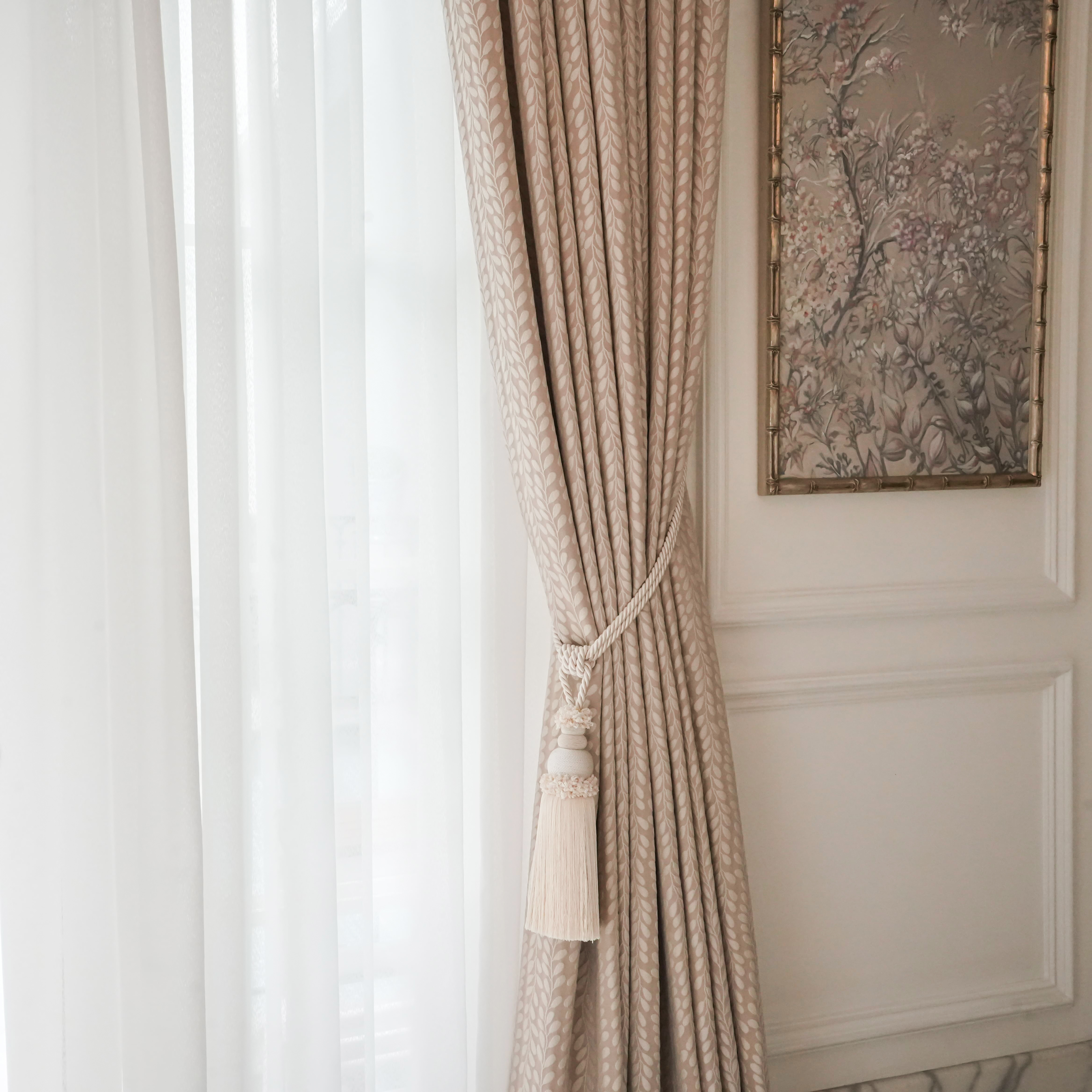 Stylish cream-patterned curtain held by a tassel tie-back, beside a soft sheer white curtain.